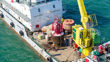 Commercial specialized vessel with a yellow crane working on a red navigational buoy in the blue ocean. Maritime safety, navigation infrastructure, and offshore maintenance business concept. © Yellow Boat