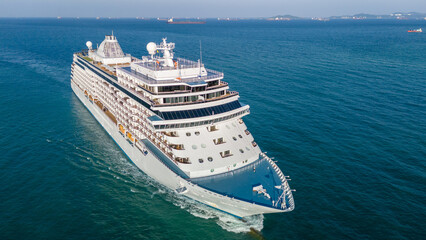 Fototapeta premium Majestic white luxury cruise ship sailing across the deep blue ocean water on a bright sunny day. Summer vacation, tropical travel destination, and global tourism industry concept.