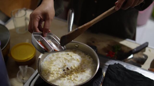 Anonymous woman cooking instant noodles or "Mie Nyemek" in a pan, stirring noodles with savory thick sauce and spices in a home kitchen