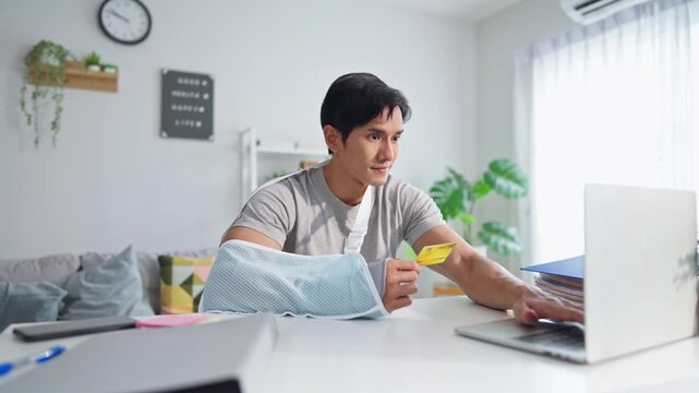 Injured Asian man with hand splint using laptop for online shopping. 