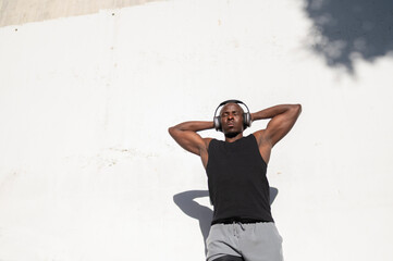 Man enjoying music and resting against a white wall after exercising