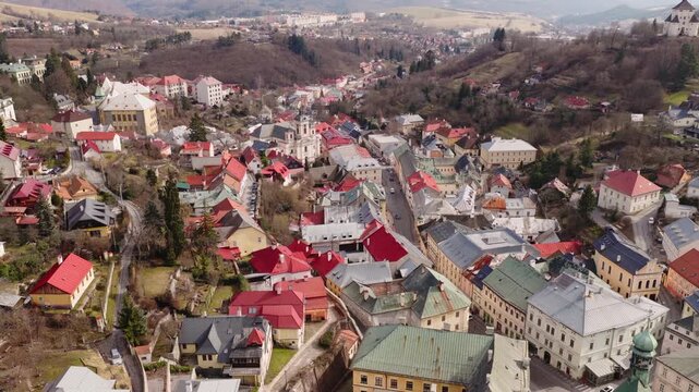 Aerial drone view of Banska Stiavnica, UNESCO heritage town in Slovakia. Historic old town, colorful rooftops, church towers and rolling hills landscape in soft daylight.