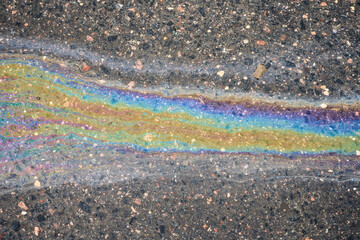 Oil slick creating an iridescent rainbow pattern on wet asphalt, showing fluid texture and pollution concept
