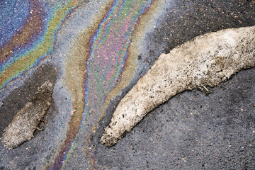 Vibrant rainbow oil slick on wet asphalt road surface with melting dirty snow, abstract pollution pattern