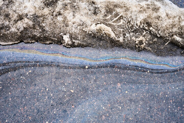 Oil slick creating beautiful yet dangerous rainbow sheen on melting snow and puddle of water on urban asphalt, representing pollution
