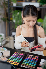 Fototapeta premium Asian woman applying make up foundation and concealer make up on face with cosmetics makeover Daily beauty routine at home.