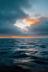 Fototapeta premium Open ocean seascape vertical view at sunrise with dramatic storm clouds parting to reveal golden light over teal rippling waves