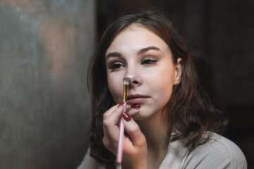 Fototapeta premium woman powders her nose with a brush, applying makeup to enhance her beauty.