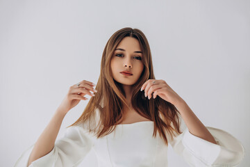 Fototapeta premium Beauty portrait of a model, a beautiful brunette girl with straight long hair in a white dress, healthy and natural on a white background