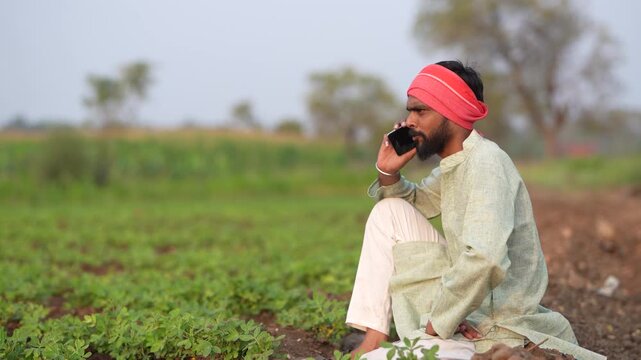 young indian farmer talking on smartphone standing at green peanut field	