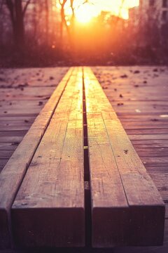 Empty wooden bench of parallel planks on a boardwalk glowing in golden sunset with scattered leaves and silhouetted trees, peaceful and nostalgic