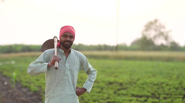 young indian farmer holding farming tool standing at field	