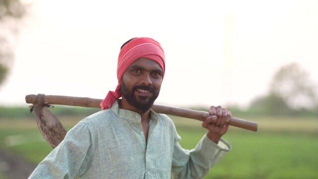 young indian farmer holding farming tool standing at field	