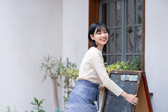 お店の前で看板を出している女性