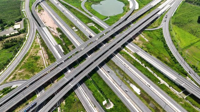 Aerial view of modern highway interchange with multilayer roads and curved ramps surrounded by green farmland, showcasing transportation infrastructure, urban development, and road network planning.
