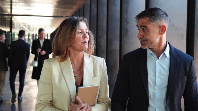 Two professionals engage in a lively discussion, sharing ideas and insights while walking together through a business district, showcasing teamwork and collaboration in a dynamic environment.