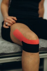 Obraz premium Woman applying kinesiology tape for knee pain support