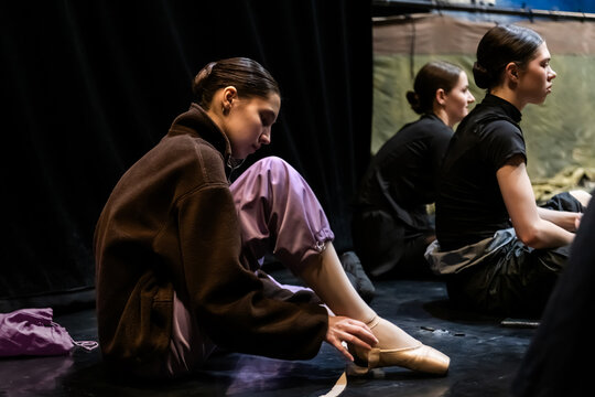 Female dancers prepare pointe shoes backstage at a ballet performance.