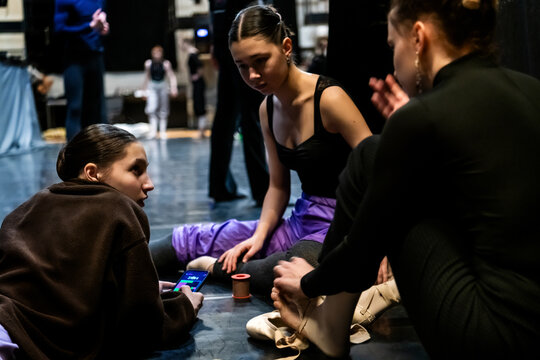 Three ballerinas adjusting pointe shoes and taping feet backstage