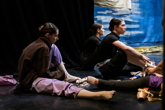 Female dancers prepare pointe shoes backstage at a ballet performance.