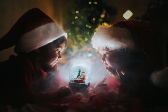 Little Children in Santa hats looking at glowing glass Christmas ball