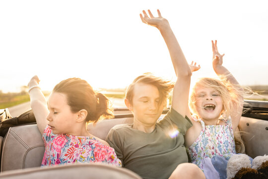 Young kids riding in convertible car on sunny day