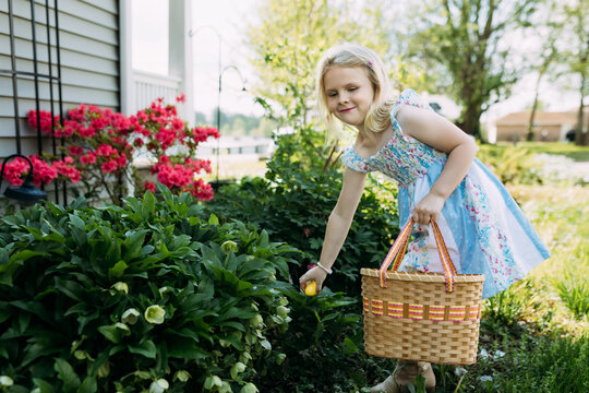 Child holding Easter basket hunting eggs in yard