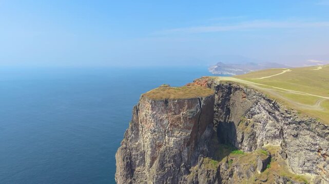Aerial view of steep rocky cliffs and a winding dirt road overlooking the Arabian Sea in Salalah, Oman.