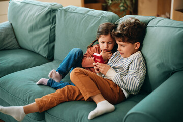 Siblings playing handheld game console on sofa © djile