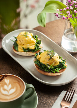 A close-up shot of two poached eggs served on toasted English muffins with a generous layer of sauteed green spinach, topped with rich yellow hollandaise sauce and fresh dill.