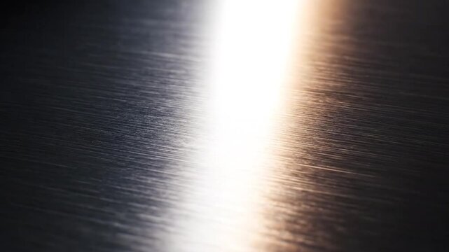 Light reflection moves across a dark brushed l surface texture.