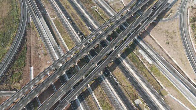 Aerial view of modern highway interchange with multilayer roads and curved ramps surrounded by green farmland, showcasing transportation infrastructure, urban development, and road network planning.