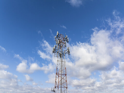 Aerial view of a cell phone tower piercing the vibrant blue sky dotted with fluffy white clouds, a stark contrast of technology against nature, Hollywood, Florida, United States.
