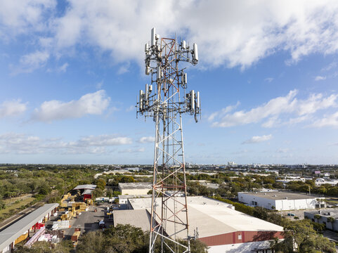 Aerial view of a towering cell phone tower piercing the skyline against a backdrop of warehouses and distant cityscapes, Hollywood, Florida, United States.