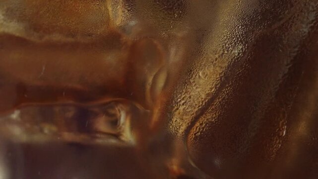 4K Macro close-up of black coffee being poured over ice cubes in a glass, Rich brown liquid flows through clear ice with dynamic splash and texture ideal for refreshing beverage and cafe concepts.