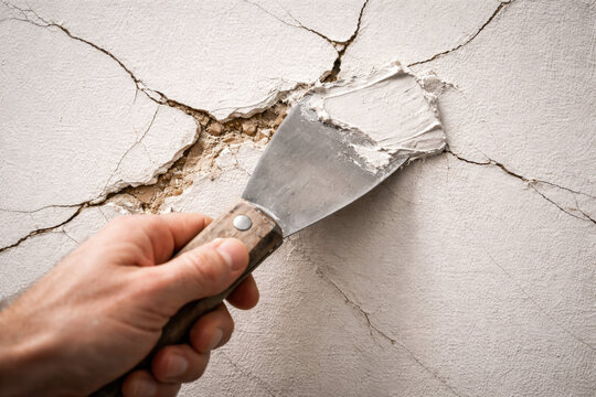 Hand applying wall filler to cracked plaster surface using a putty knife, illustrating home renovation, drywall repair, and interior maintenance work.