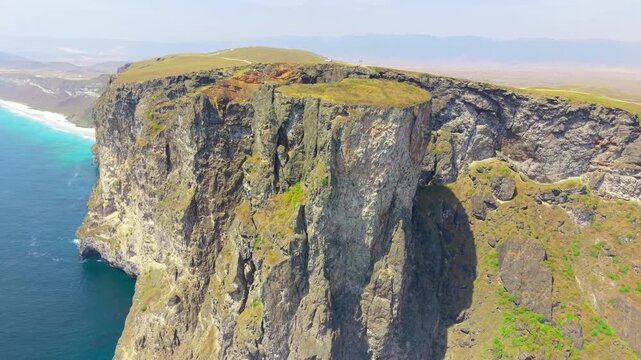 Aerial view of massive limestone cliffs and rocky coastline overlooking the blue waters of the Arabian Sea in Shaat, Salalah, Oman.