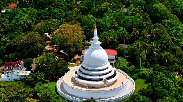 Aerial view of the Japanese Peace Pagoda at Rumassala, a white stupa on a lush green hilltop surrounded by tropical forest.