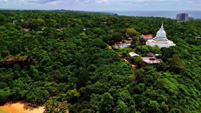 Aerial view of the Japanese Peace Pagoda at Rumassala, with a white stupa visible in the distance amid dense green forest and hillside.