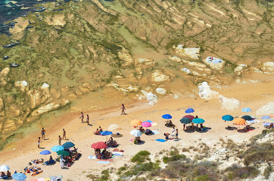 Crowded beach with colorful sun umbrellas at the base of the white marl cliffs of Scala dei Turchi, Realmonte, Sicily, Italy.