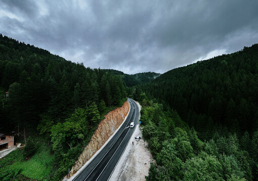 Aerial view of a road slicing through dense evergreen forests under a brooding sky, Romanija, Republika Srpska, Bosnia and Herzegovina.
