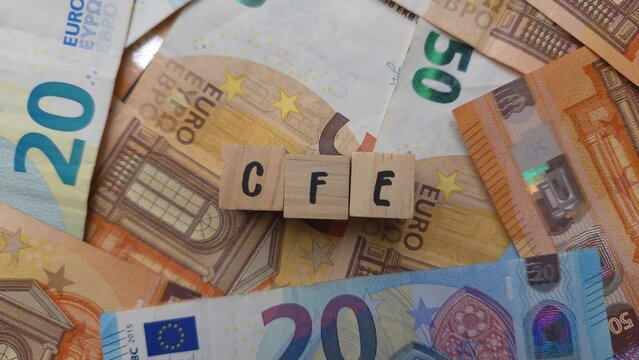 CFE acronym made of wooden letter cubes on pile of Euro banknotes. Cotisation Fonci&egrave;re des Entreprises (Business Property Tax)