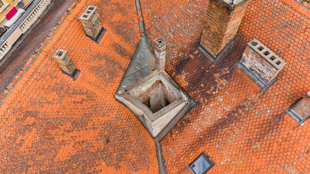 Aerial view of the intricate patterns and textures of weathered terracotta tiles, punctuated by aged brick chimneys and a unique rooftop structure, Sremska Mitrovica, Vojvodina, Serbia.