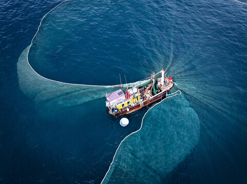 Aerial view of a fishing boat encircled by a vast net casts a mesmerizing pattern against the deep blue sea, Tuy Hoa, Phu Yen, Vietnam.