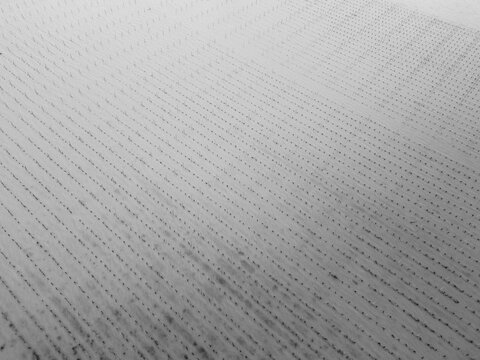 Aerial view of a snow-covered field, the stark white surface etched with dark, parallel lines creating a mesmerizing pattern, Portets, Nouvelle-Aquitaine, France.