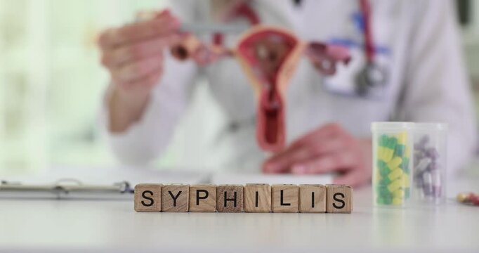 Wooden blocks spell word Syphilis on desk near uterus model and pills. Doctor lifts swab preparing test sample for infection screening in clinic
