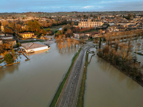 Cadillac-sur-Garonne, France - 20 February 2026: Aerial view of floodwaters engulfing buildings and roads, with a bridge barely visible amidst the muted tones of submerged landscapes.