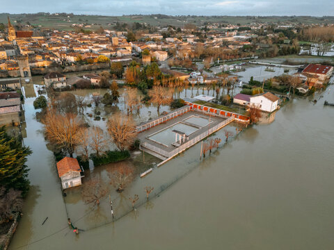 Cadillac-sur-Garonne, France - 20 February 2026: Aerial view of a town partially submerged in muddy floodwaters, with rooftops peeking through, reflecting the somber sky.