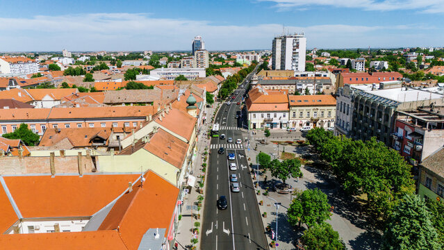 Aerial view of sun-drenched streets lined with terracotta roofs and modern buildings, the vibrant cityscape punctuated by lush greenery, Pancevo, Vojvodina, Serbia.