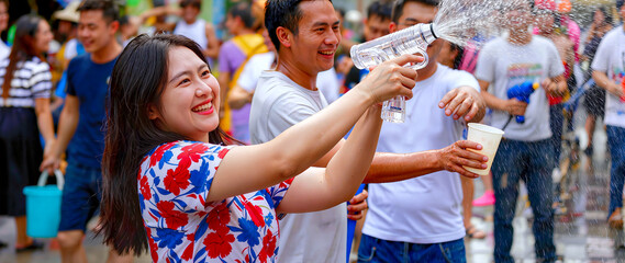 Naklejka premium Cheerful young Asian woman enjoying Songkran water festival in Thailand, playing with water gun among crowd, traditional Thai New Year celebration, , panoramic banner with copy space.